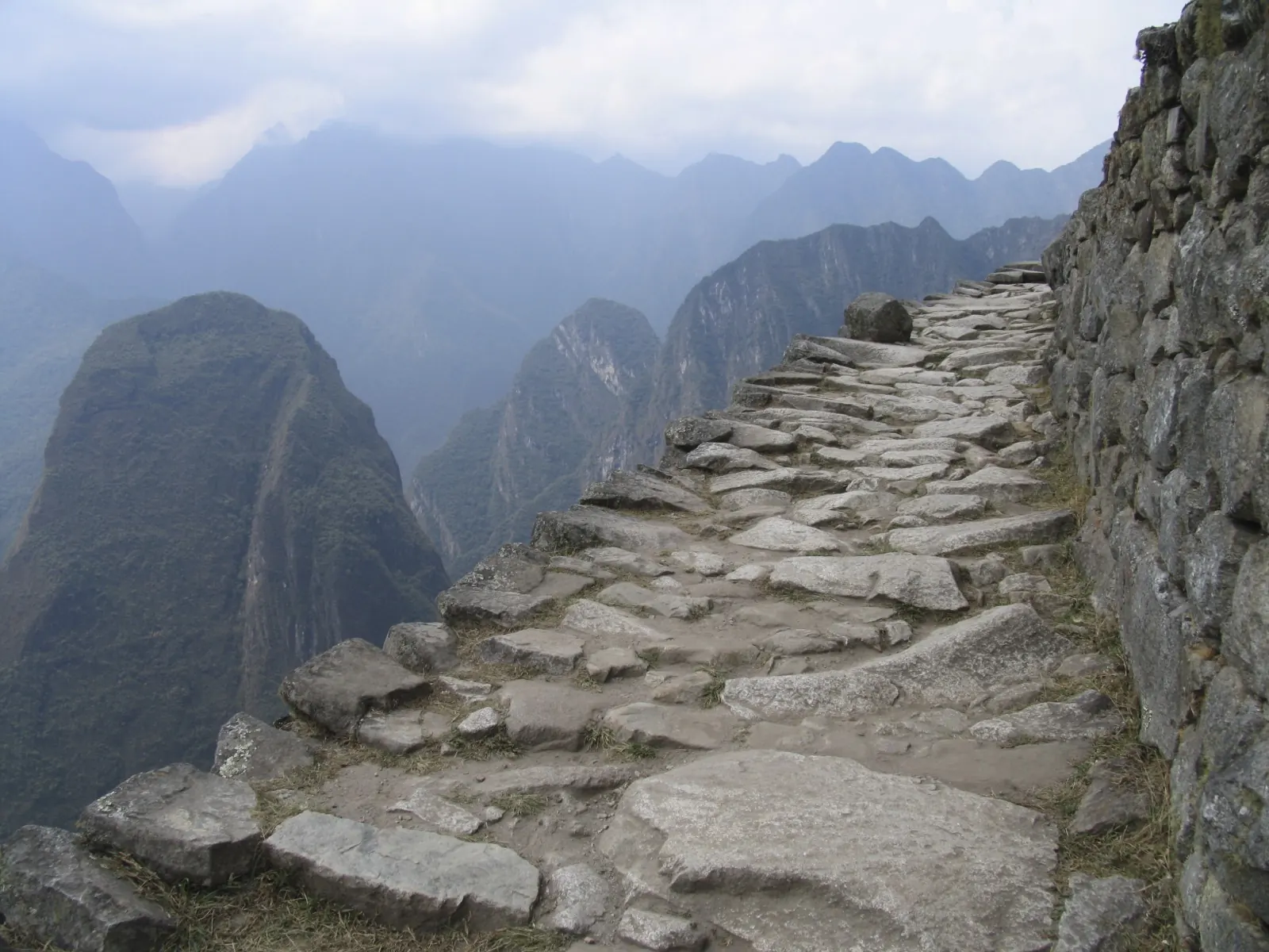Original stone path of the Inca Trail hugging a mountainside above the valley